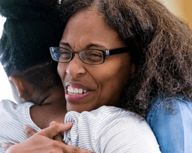 Woman wearing glasses hugging someone excitedly