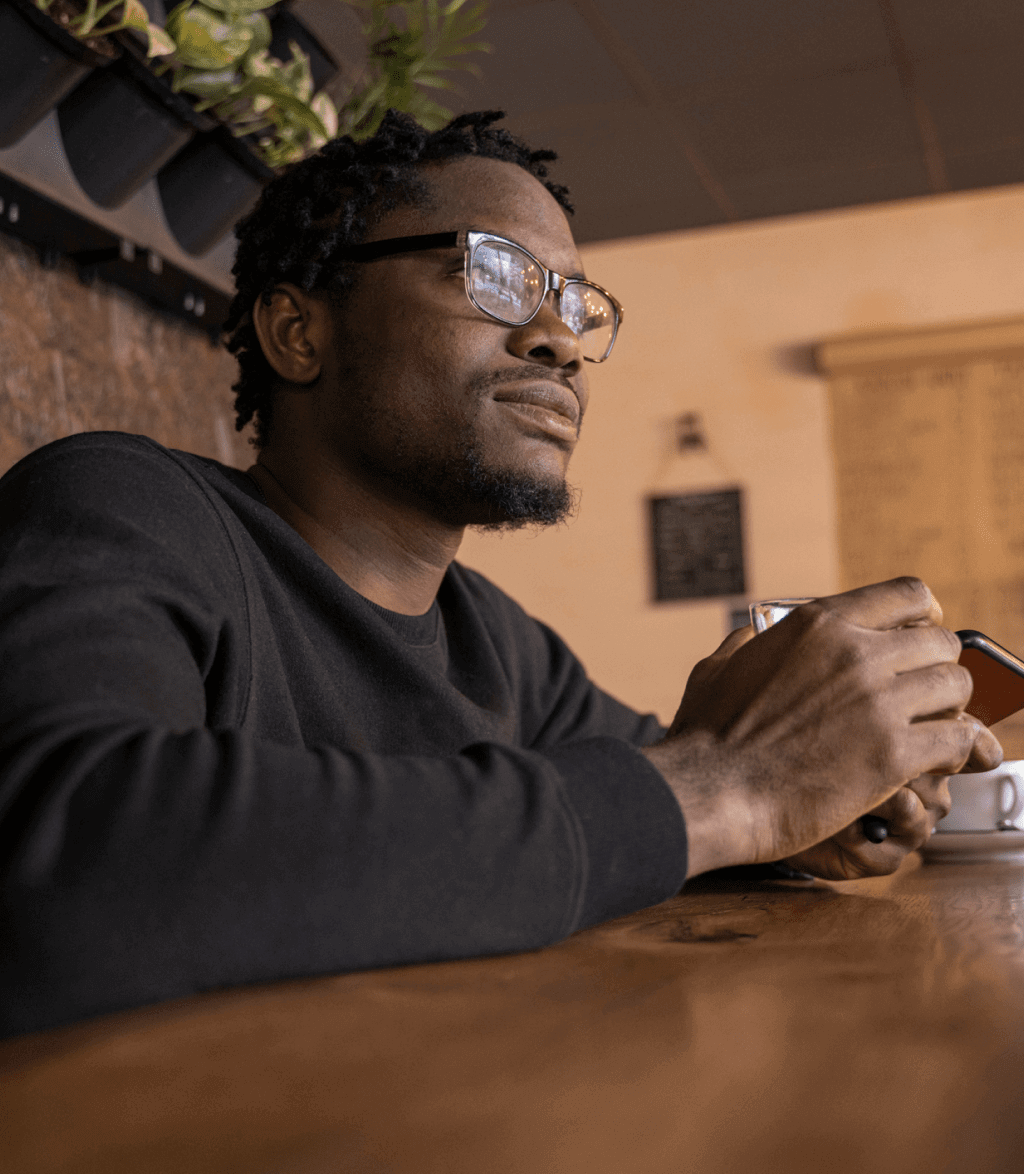 Man wearing glasses sitting at a table holding his phone